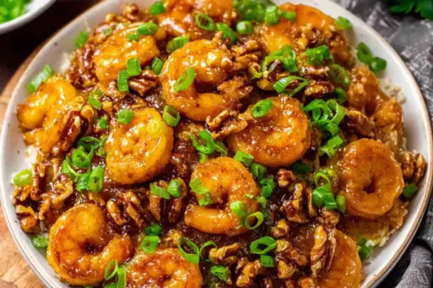 Close-up of crispy Honey Walnut Shrimp topped with chopped green onions and candied walnuts, served over rice on a white plate.