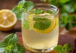 Glass of refreshing lemon balm tea with lemon slices and fresh lemon balm leaves on a wooden table