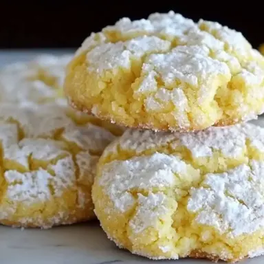 Close-up of freshly baked lemon crinkle cookies dusted with powdered sugar, showing their soft, cracked tops and vibrant yellow color.