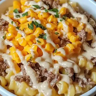 Bowl of Loaded Cheddar Ranch Beef with curly pasta, ground beef, cheddar cheese, sweet corn, ranch drizzle, and fresh herbs on top.