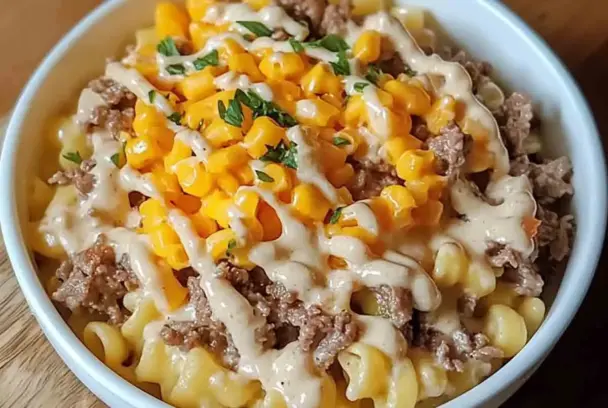Bowl of Loaded Cheddar Ranch Beef with curly pasta, ground beef, cheddar cheese, sweet corn, ranch drizzle, and fresh herbs on top.