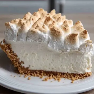 A slice of Marshmallow Whip Cheesecake Heaven with a golden graham cracker crust and toasted marshmallow topping, served on a white plate.