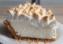 Close-up of a slice of Marshmallow Whip Cheesecake Heaven with a toasted marshmallow topping and graham cracker crust on a white plate.