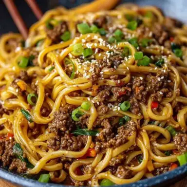 A close-up of Mongolian Ground Beef Noodles served in a bowl, topped with chopped green onions and sesame seeds, showcasing saucy noodles and crumbled beef in a rich brown glaze.
