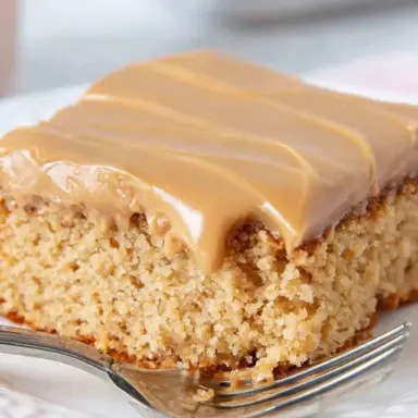 A thick square of moist peanut butter Texas sheet cake with creamy peanut butter frosting, served on a white plate with a fork.