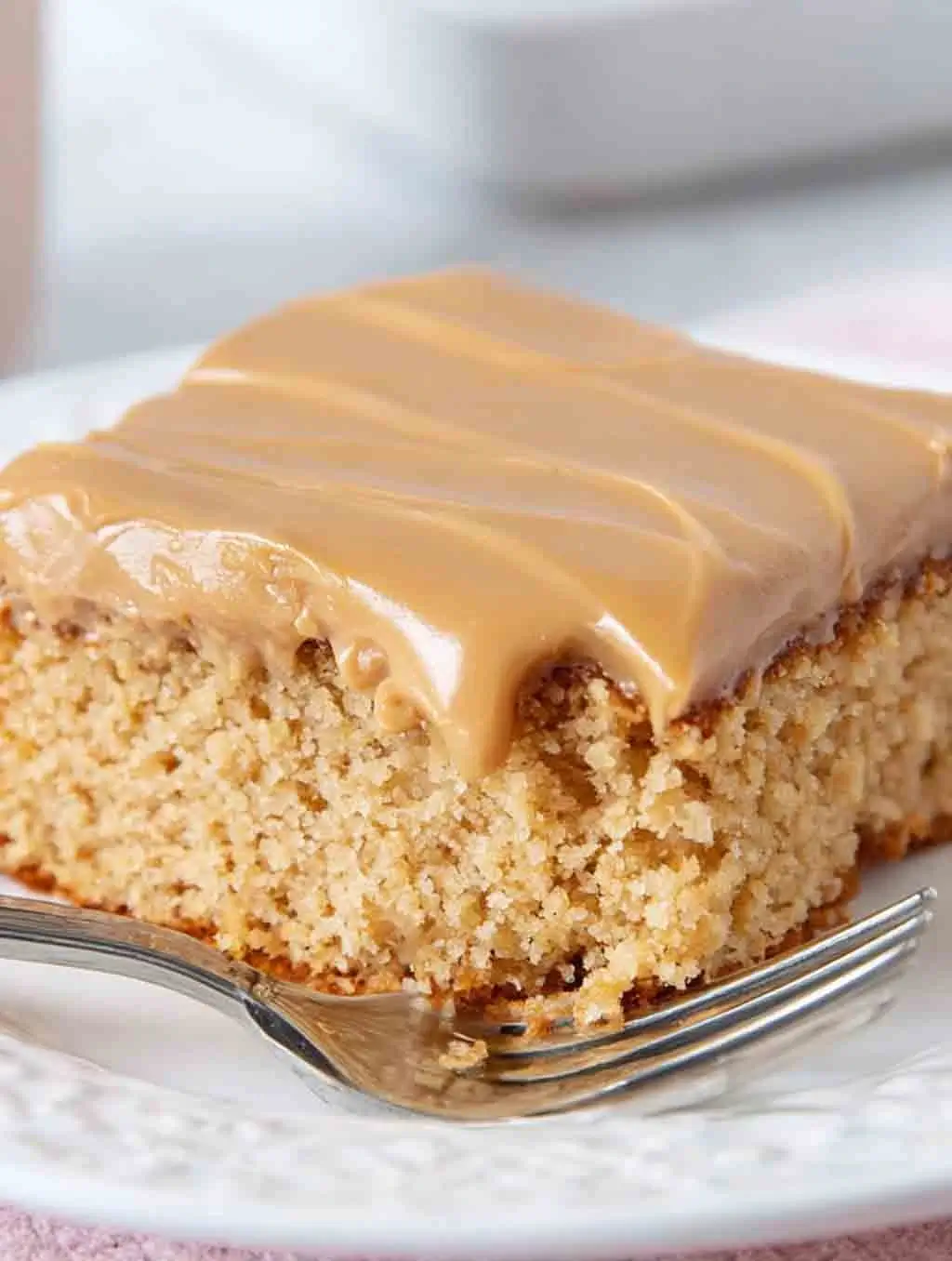 A thick square of moist peanut butter Texas sheet cake with creamy peanut butter frosting, served on a white plate with a fork.