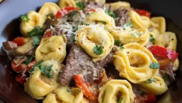 Close-up of Philly Cheesesteak Tortellini in a bowl, with creamy cheese sauce, sautéed red peppers, onions, mushrooms, and tender steak slices