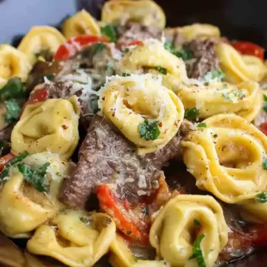 Close-up of Philly Cheesesteak Tortellini in a bowl, with creamy cheese sauce, sautéed red peppers, onions, mushrooms, and tender steak slices