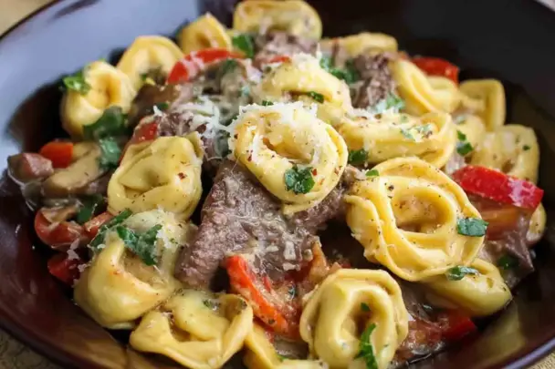 Close-up of Philly Cheesesteak Tortellini in a bowl, with creamy cheese sauce, sautéed red peppers, onions, mushrooms, and tender steak slices