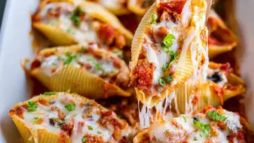 Close-up of cheesy pizza stuffed pasta shells filled with pepperoni, melted mozzarella, and pizza sauce, garnished with fresh parsley in a white baking dish.