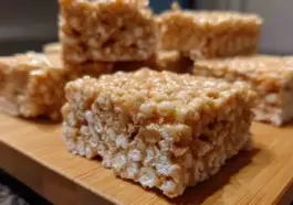 Close-up of homemade rice crispy treats stacked on a wooden board, showing their gooey texture and crispy cereal layers.