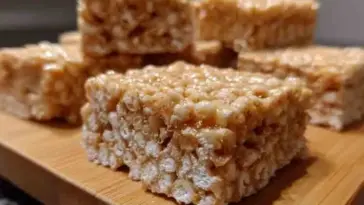 Close-up of homemade rice crispy treats stacked on a wooden board, showing their gooey texture and crispy cereal layers.