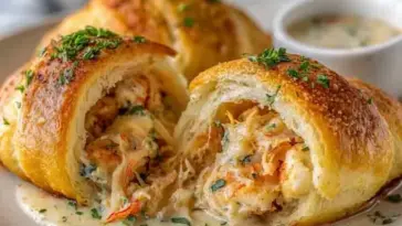 Golden-brown crescent roll bombs stuffed with creamy shrimp and crab filling, topped with herbs and served with a side of dipping sauce.