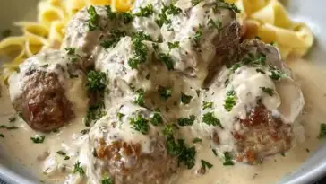 Close-up of creamy Swedish meatballs garnished with fresh parsley, served over egg noodles with rich white gravy, all made in a slow cooker.