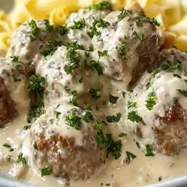 Close-up of creamy Swedish meatballs garnished with fresh parsley, served over egg noodles with rich white gravy, all made in a slow cooker.