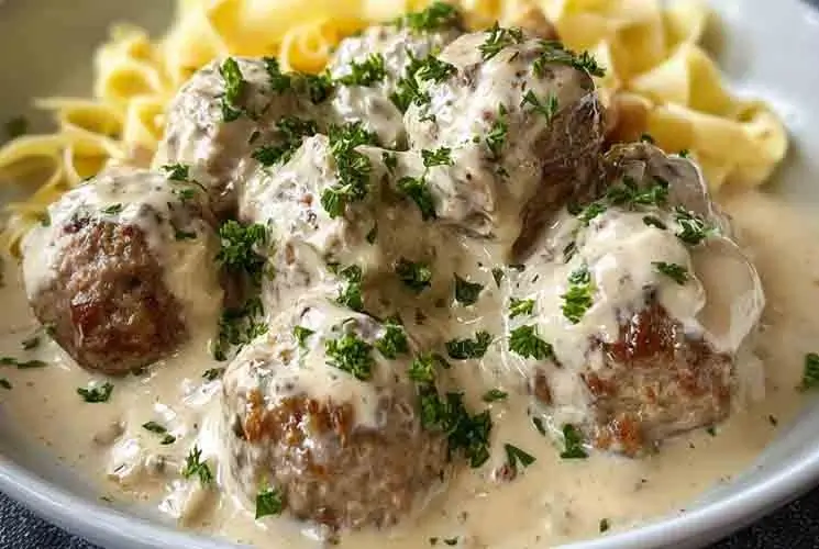 Close-up of creamy Swedish meatballs garnished with fresh parsley, served over egg noodles with rich white gravy, all made in a slow cooker.
