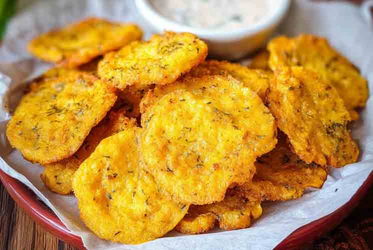 Close-up of crispy Southern Fried Squash slices on a plate lined with parchment paper, with a bowl of dipping sauce in the background.