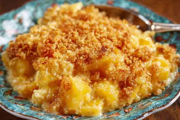 A serving of golden-brown Southern Pineapple Casserole on a teal floral plate, showcasing juicy pineapple chunks and a crispy cracker topping with a spoon in the background.