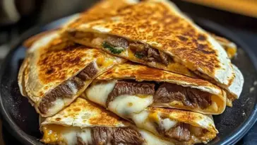 A stack of golden, crispy steak cheese quesadillas filled with juicy beef and melted cheese, served on a dark plate for a comforting and satisfying meal.