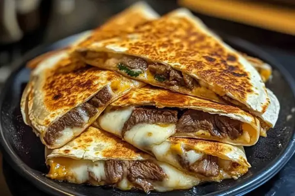 A stack of golden, crispy steak cheese quesadillas filled with juicy beef and melted cheese, served on a dark plate for a comforting and satisfying meal.