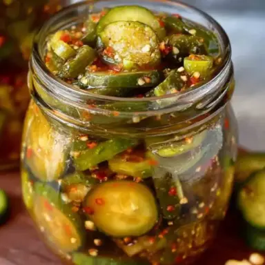 A close-up of a mason jar filled with homemade Sweet Heat Pickles, featuring sliced cucumbers, red pepper flakes, and jalapeños in a vibrant spicy brine.