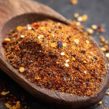 Close-up of a wooden spoon filled with vibrant homemade taco seasoning made from a blend of chili powder, cumin, paprika, and red pepper flakes.