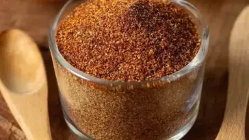 Glass jar filled with a homemade taco seasoning blend made from ground spices like chili powder, cumin, garlic powder, and paprika, with wooden spoons nearby.