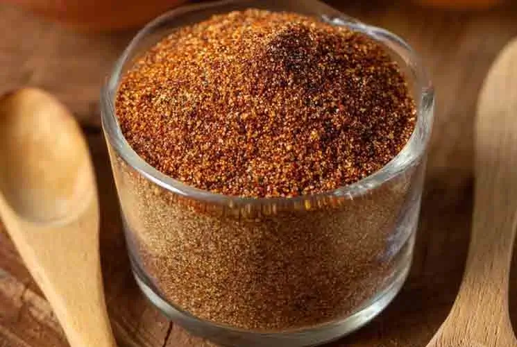 Glass jar filled with a homemade taco seasoning blend made from ground spices like chili powder, cumin, garlic powder, and paprika, with wooden spoons nearby.