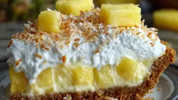 A slice of Tropical Pineapple Paradise Pie with graham cracker crust, creamy pineapple filling, whipped topping, toasted coconut, and pineapple chunks on top.