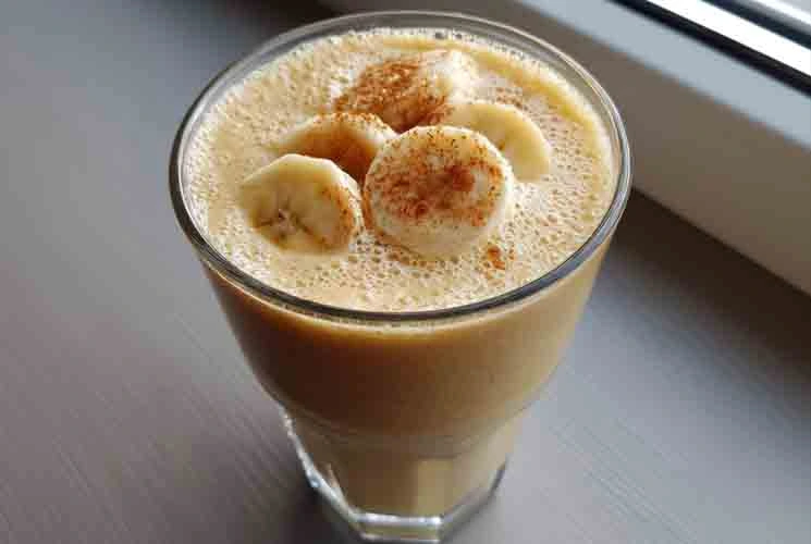 Glass of weight-loss banana smoothie topped with banana slices and cinnamon, placed on a window-side table with soft natural light.