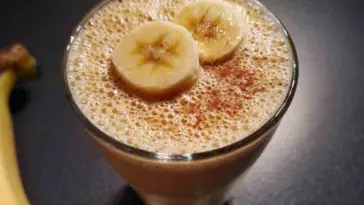 Banana smoothie topped with sliced banana and cinnamon in a clear glass, photographed on a dark surface—perfect for a healthy, fat-burning breakfast idea.