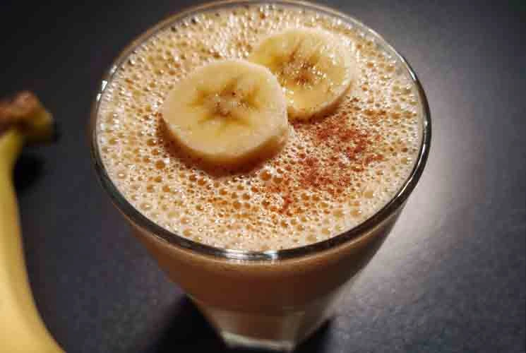 Banana smoothie topped with sliced banana and cinnamon in a clear glass, photographed on a dark surface—perfect for a healthy, fat-burning breakfast idea.