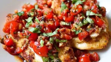 Pan-seared chicken breasts topped with a colorful bruschetta mix of diced cherry tomatoes, garlic, chopped basil, and balsamic glaze on a white plate.