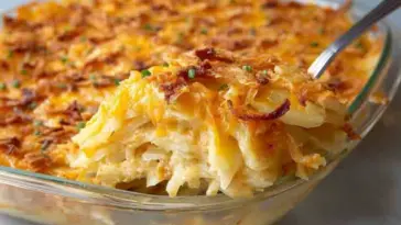 Glass dish of baked cheesy potato casserole with layers of creamy potatoes, melted cheddar, and crispy golden topping being scooped out with a spoon.