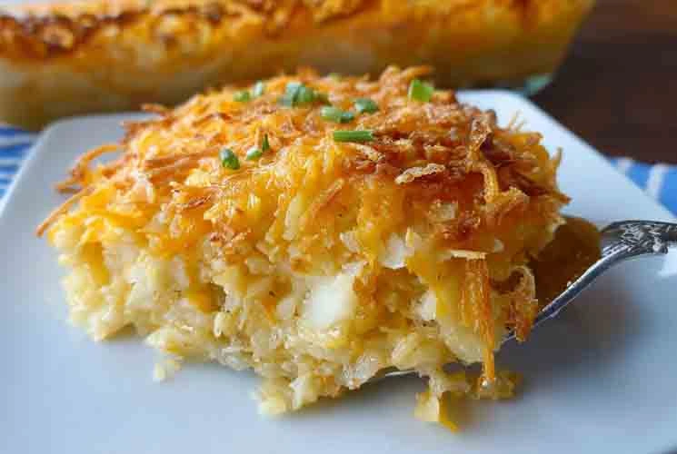 Close-up of a sliced serving of cheesy potato casserole on a white plate, showing crispy golden topping, melted cheese, and tender shredded potatoes.