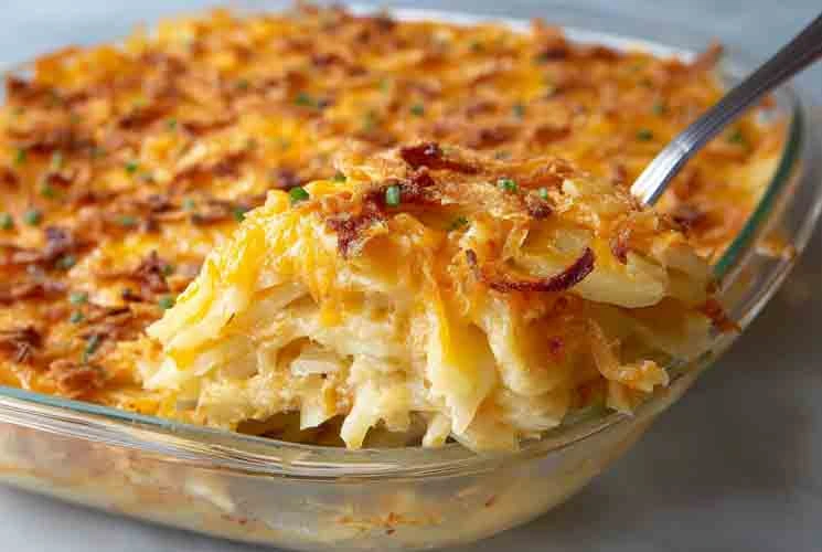Glass dish of baked cheesy potato casserole with layers of creamy potatoes, melted cheddar, and crispy golden topping being scooped out with a spoon.