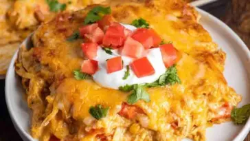 Close-up of a cheesy chicken fajita casserole slice topped with sour cream, diced tomatoes, and chopped cilantro, served on a white plate.