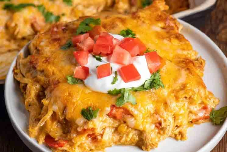 Close-up of a cheesy chicken fajita casserole slice topped with sour cream, diced tomatoes, and chopped cilantro, served on a white plate.