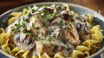 Close-up of creamy chicken mushroom stroganoff served over egg noodles, garnished with chopped parsley and sautéed mushrooms in a bowl