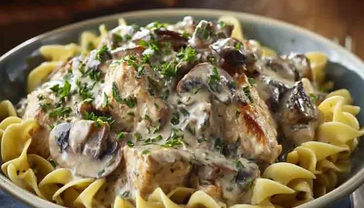 Close-up of creamy chicken mushroom stroganoff served over egg noodles, garnished with chopped parsley and sautéed mushrooms in a bowl