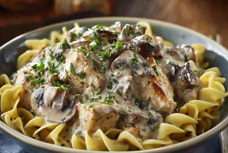 Close-up of creamy chicken mushroom stroganoff served over egg noodles, garnished with chopped parsley and sautéed mushrooms in a bowl