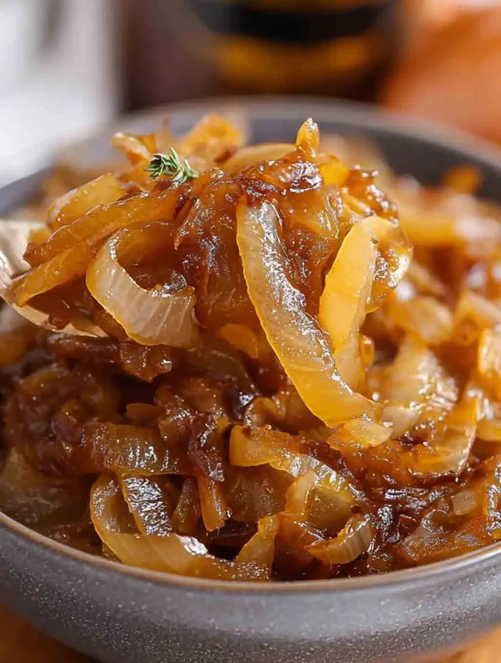 Close-up of tender, golden CrockPot caramelized onions served in a bowl, glistening with rich, sweet flavor and garnished with a sprig of thyme.