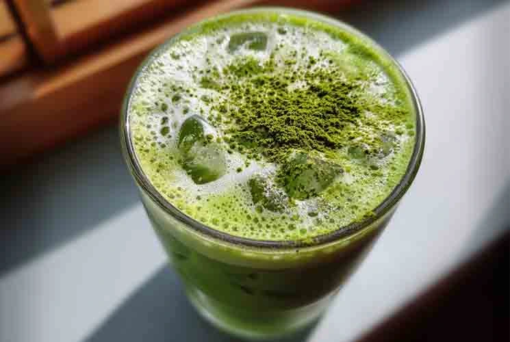 Top view of a vibrant iced matcha latte topped with bright green matcha powder and foam, served in a tall glass with ice cubes.