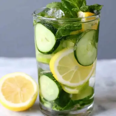 A tall glass filled with refreshing mint cucumber lemon water, featuring lemon slices, cucumber rounds, fresh mint leaves, and ice cubes.