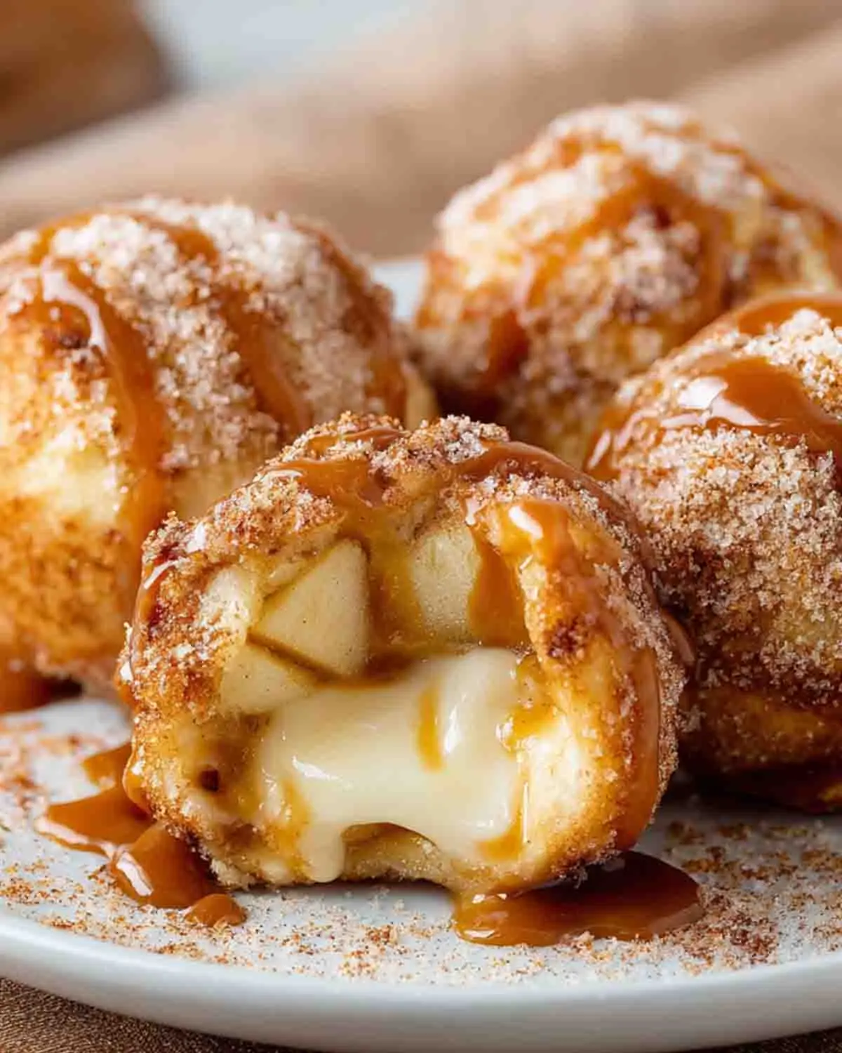 Caramel Apple Pie Bombs with gooey melted caramel and apple filling inside, coated in cinnamon sugar and drizzled with caramel sauce, close-up on a white plate