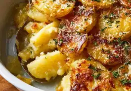 Delmonico potatoes recipe in a white baking dish with creamy sauce, golden melted cheese, crispy edges, and fresh herbs on top