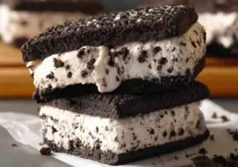 Close-up of a homemade Oreo ice cream sandwich with thick cookies and creamy cookies-and-cream ice cream filling, slightly melting and stacked on parchment paper.