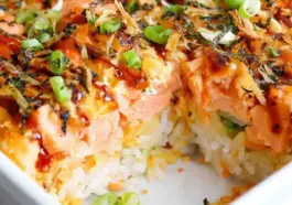 Close-up of creamy salmon sushi bake with fluffy rice layers, drizzled spicy mayo, furikake seasoning, and fresh green onions in a baking dish