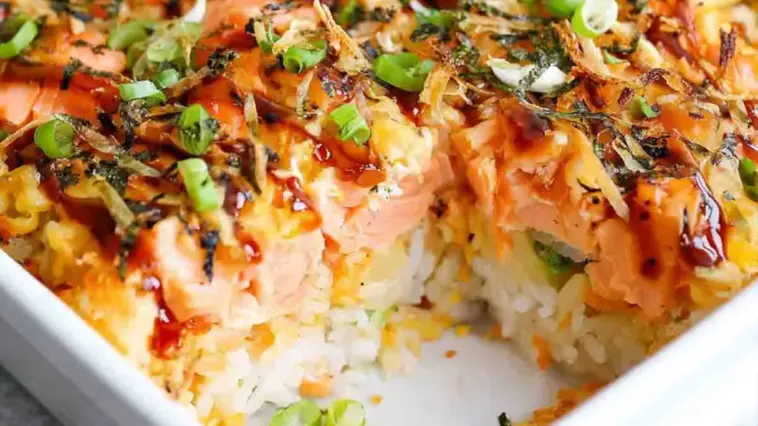 Close-up of creamy salmon sushi bake with fluffy rice layers, drizzled spicy mayo, furikake seasoning, and fresh green onions in a baking dish