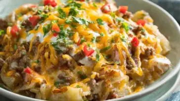 Slow cooker cowboy potato casserole with ground beef, melted cheddar cheese, diced potatoes, and fresh herbs in a creamy sauce